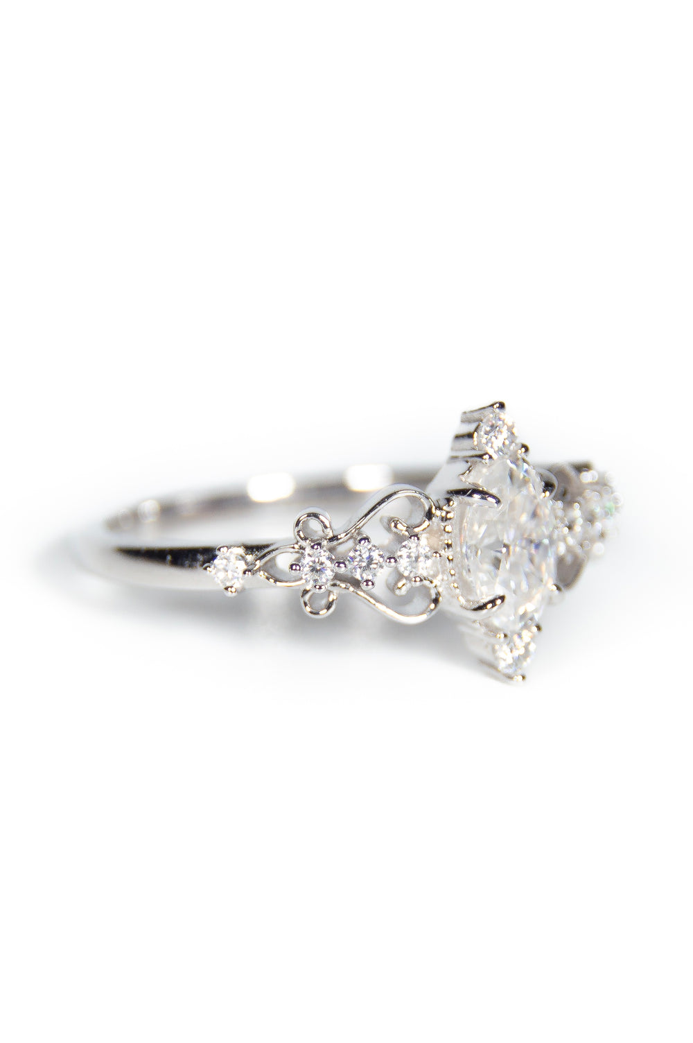 Anello di fidanzamento in oro bianco con diamante centrale brillante di grande luminosità, accompagnato da una fila di diamanti più piccoli su ogni lato. La montatura delicata presenta dettagli floreali intagliati, creando un design sofisticato e romantico.